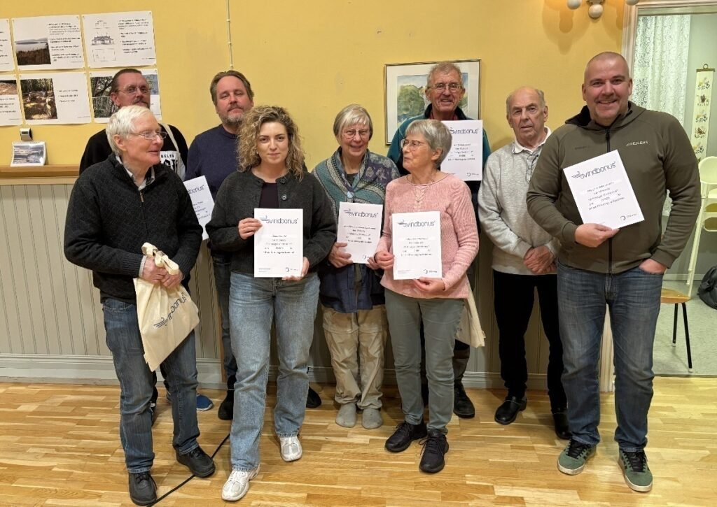 Gruppbild på representanter från de vinnande föreningarna som stolta visar upp sina diplom och tygpåsar med Vindbonus-logotypen i en föreningslokal
